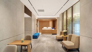 A modern hotel lobby with a reception desk, seating area, and a view of the city.