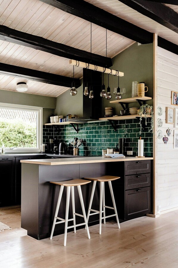 A kitchen with a wooden ceiling, green tiled backsplash, and a bar stool. - Sea view and relaxation in Mols Hills (Rønde)