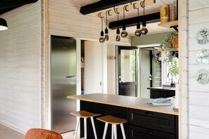 A modern kitchen with a wooden countertop, two stools, a stainless steel refrigerator, and hanging light fixtures. - Sea view and relaxation in Mols Hills (Rønde)
