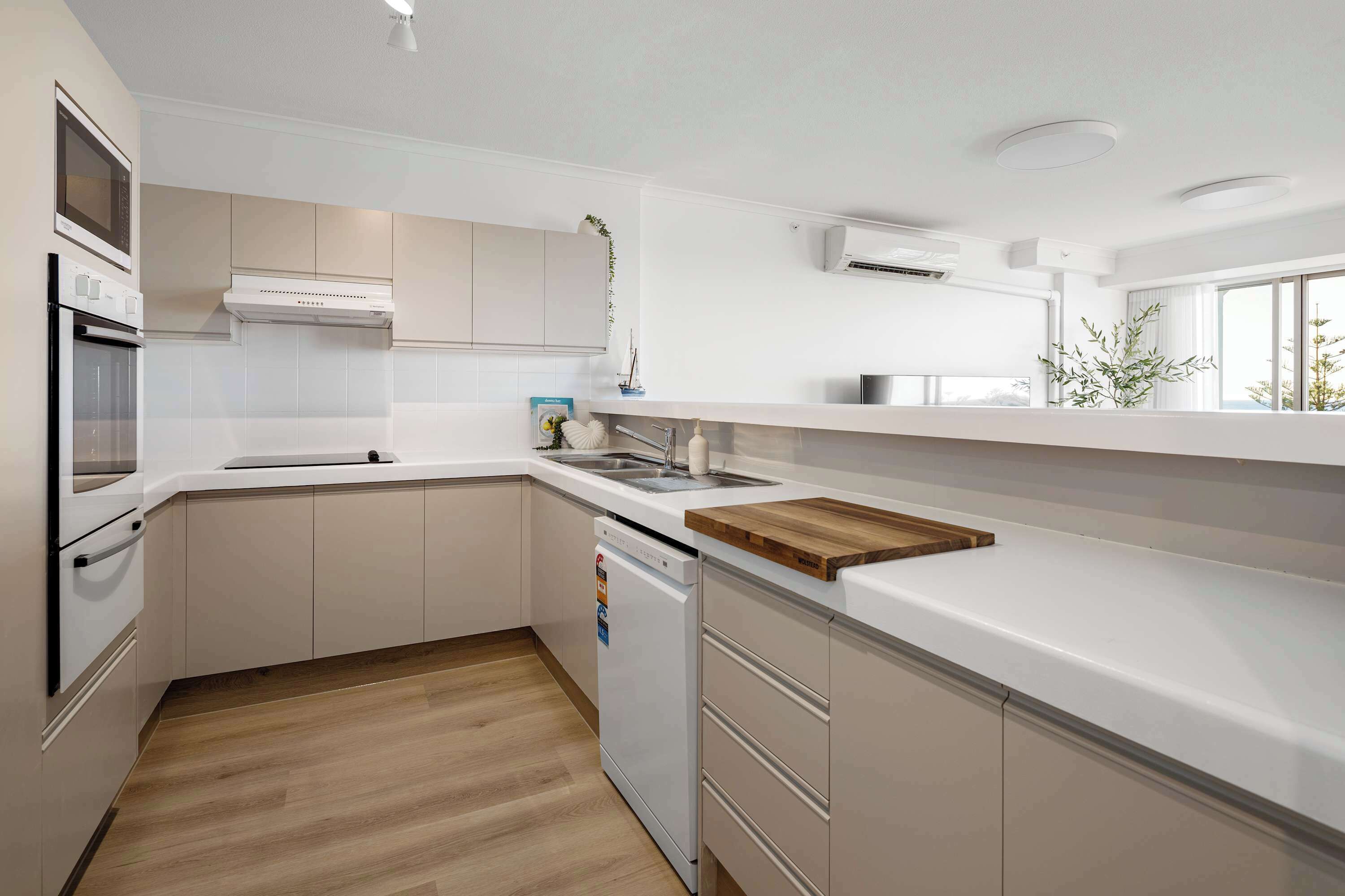 A modern kitchen with white cabinetry, a dishwasher, a wooden countertop, and a window providing natural light.