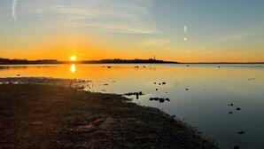 En rolig sø i solnedgang med klar himmel, stille vand og en fjer beliggende kystlinje.