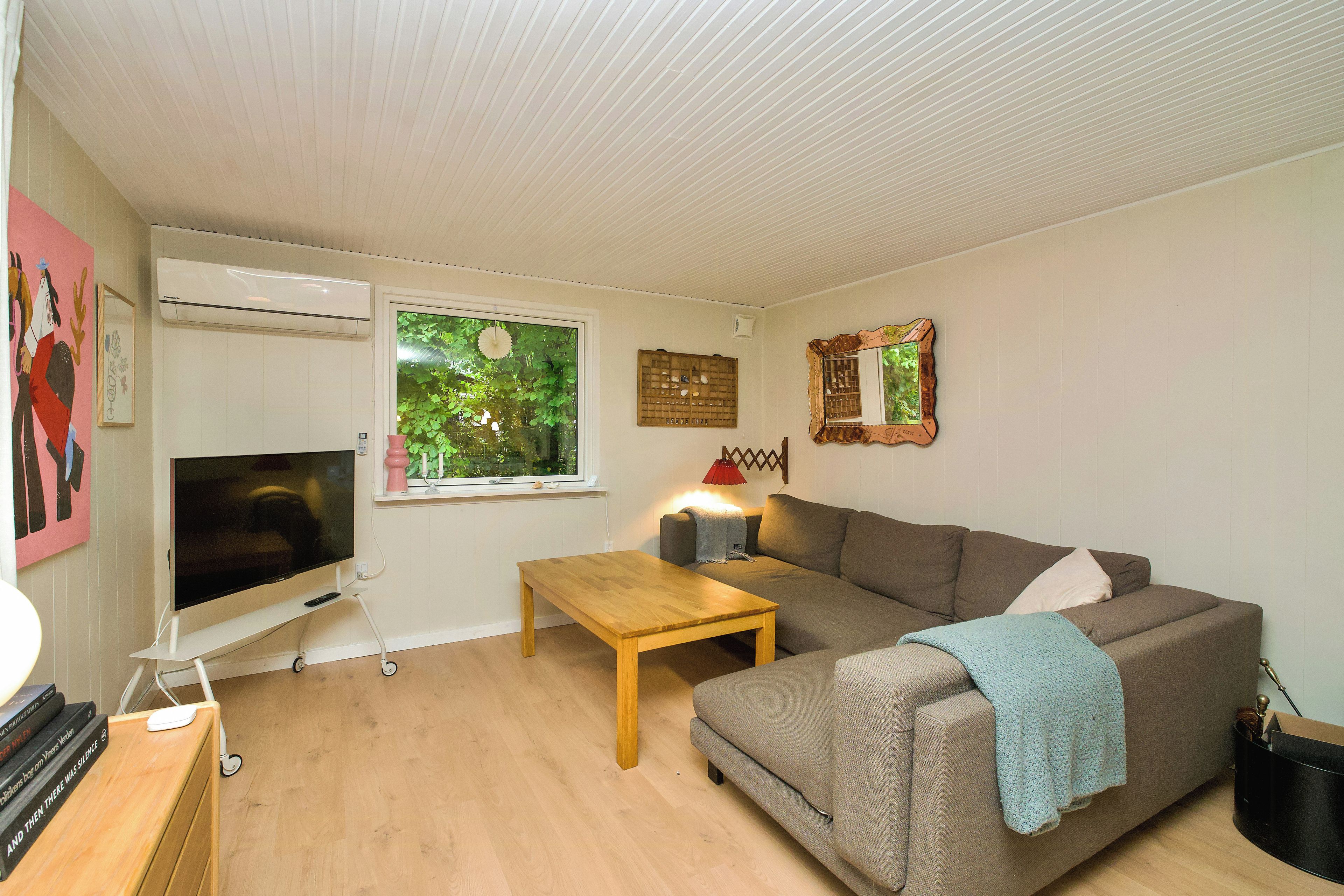 Een woonkamer met een flatscreen televisie, een houten salontafel, een bank en een raam met uitzicht op groen.