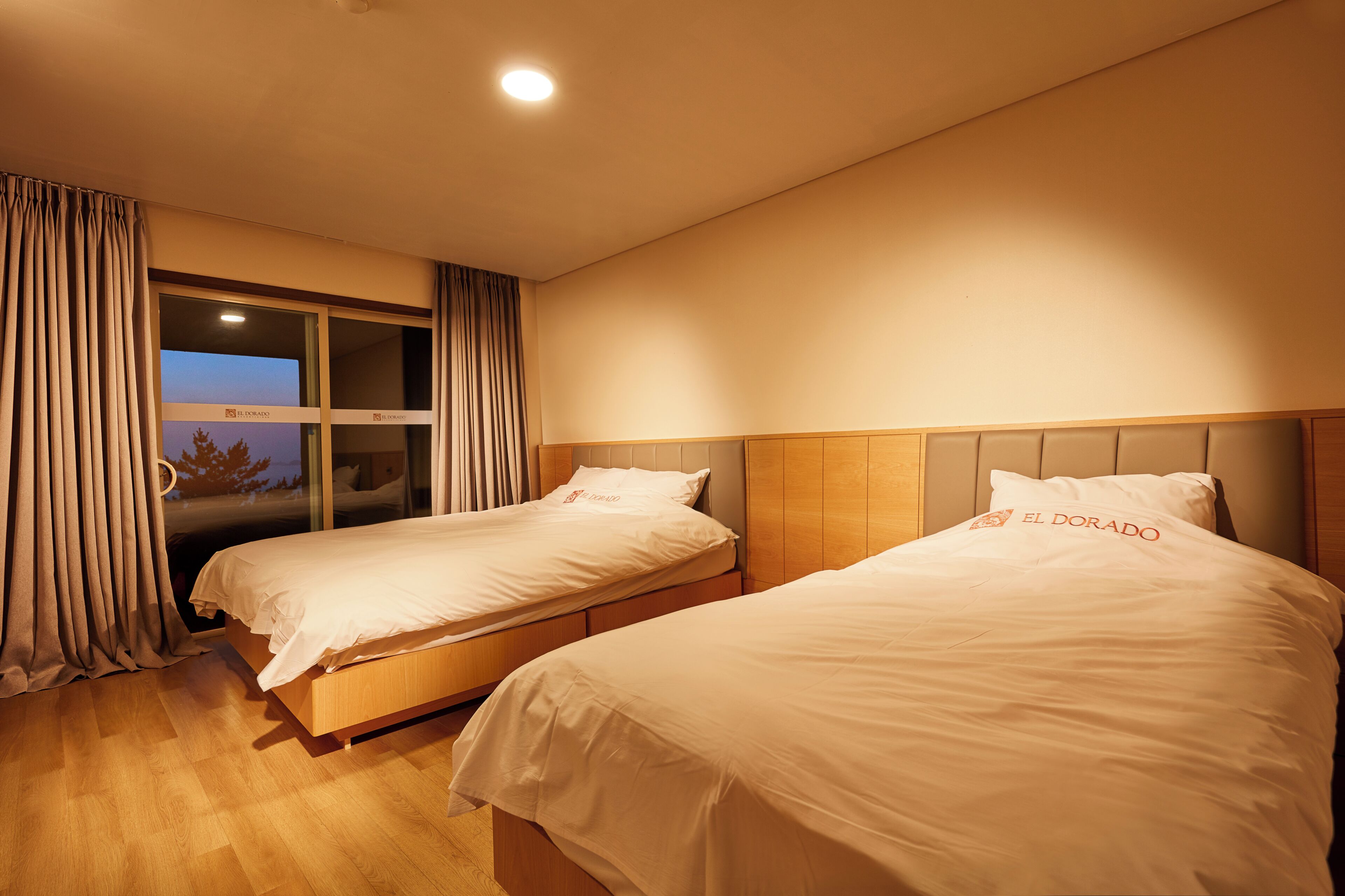 A hotel room with two beds, a window with curtains, and a view of the outdoors.