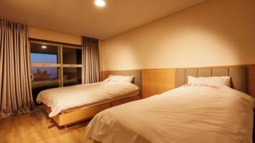 A hotel room with two beds, a window with curtains, and a view of the outdoors.