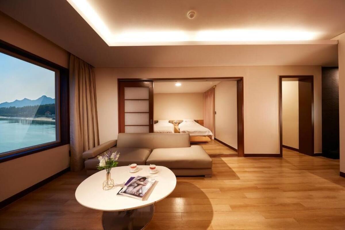 A modern hotel room with a large window, a sofa, a bed, and a small table with a vase and magazine.