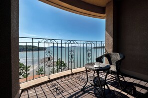 Un balcón con vista a la playa y al mar, una silla de mimbre y una mesita con una taza.