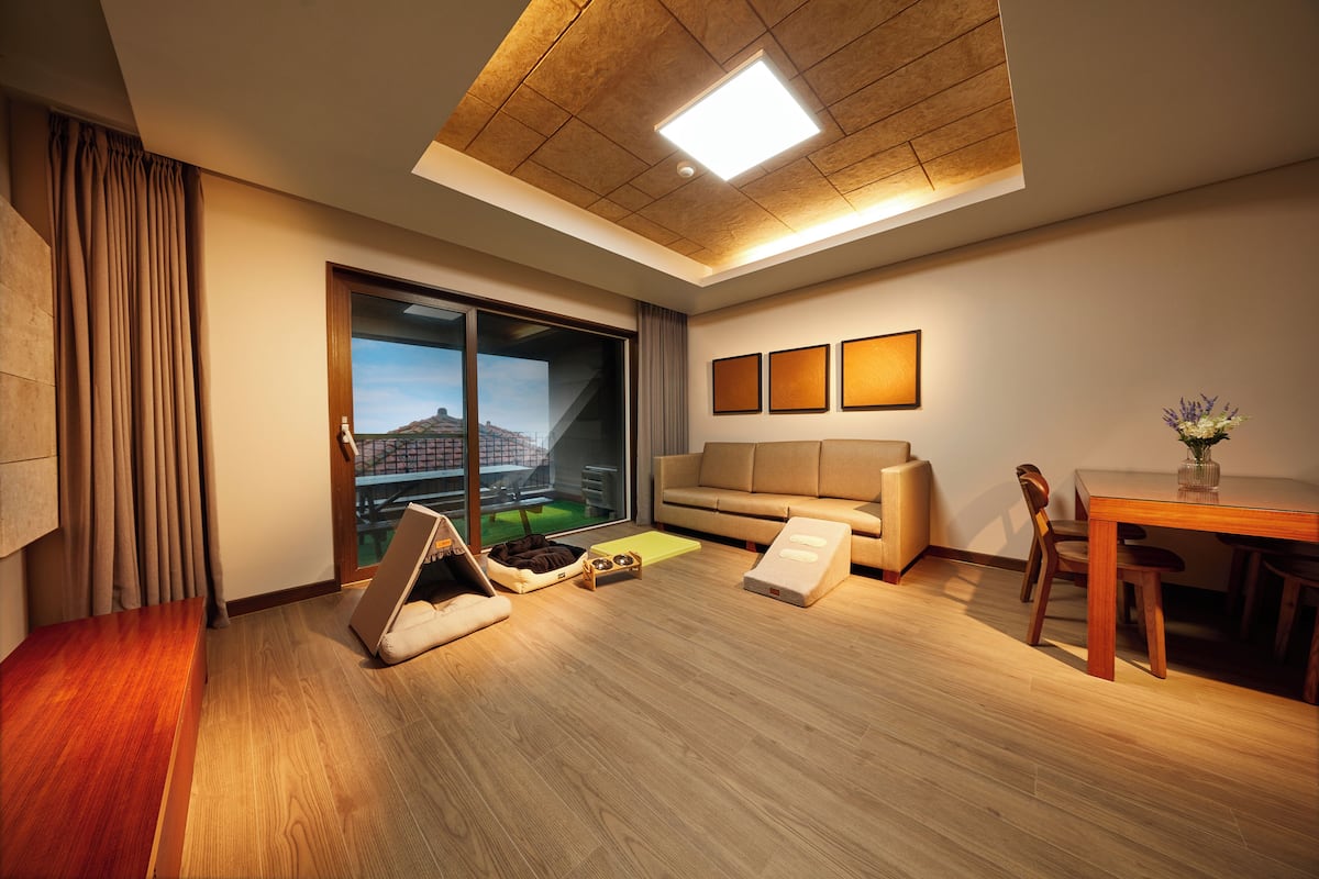 A modern living room with a sofa, dining table, and a view of a cityscape through large windows.