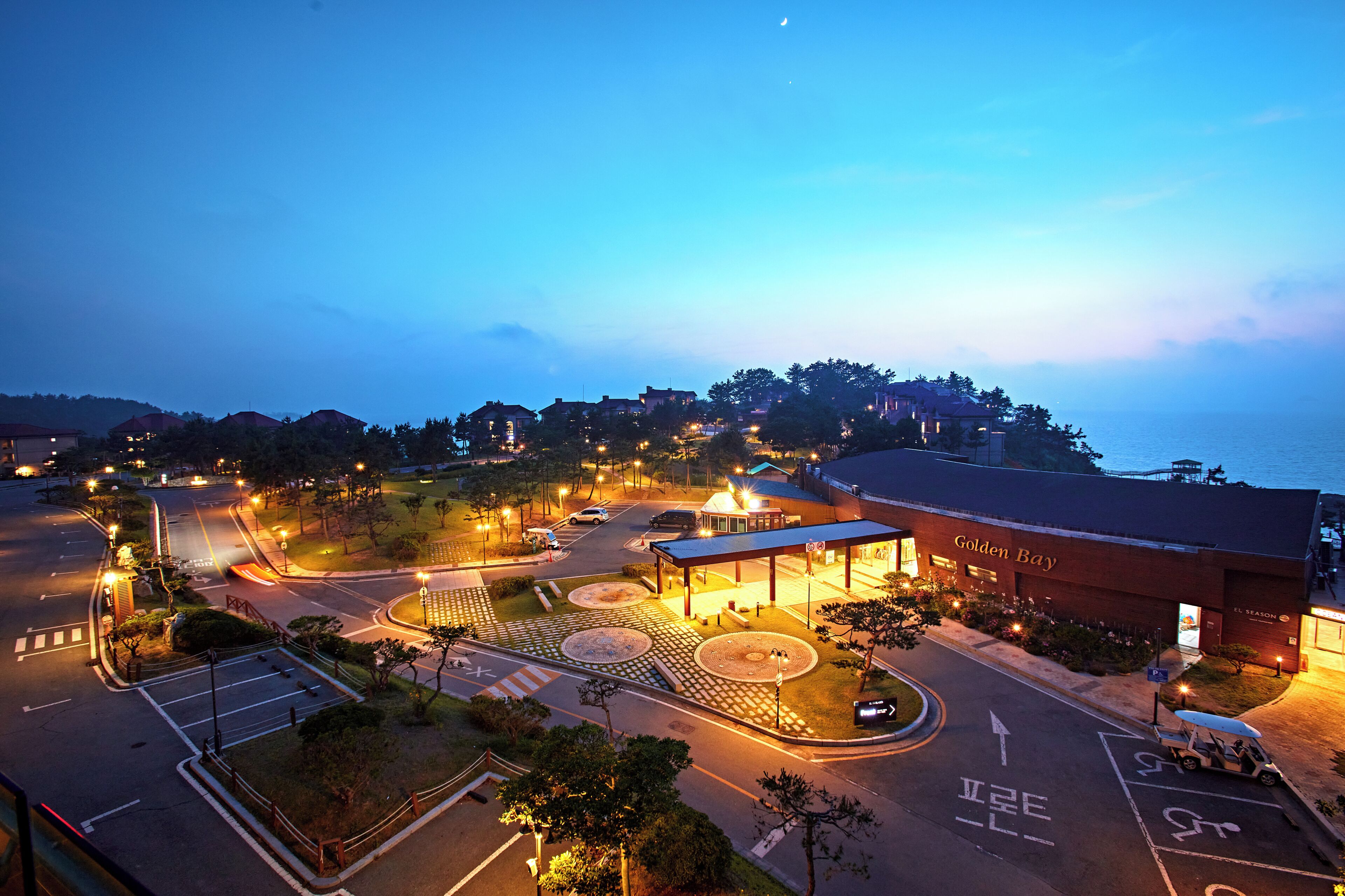 A hotel with a roundabout, parking area, and a view of the sea.