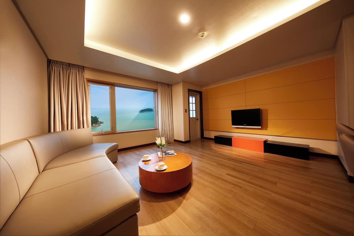 A modern living room with a sofa, a coffee table, a TV, and a large window with a view.