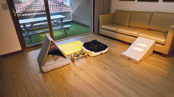 Ein Zimmer mit einer Couch, einem Haustierbett, einer Futterstelle für Haustiere und einem Fenster mit Blick auf eine Terrasse.
