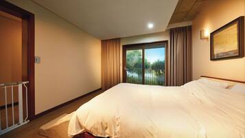 A bedroom with a large bed, a window with curtains, a door, and a framed picture on the wall.