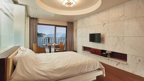 Habitación de hotel con cama, televisión, una pequeña mesa con sillas y un balcón con vista al mar.