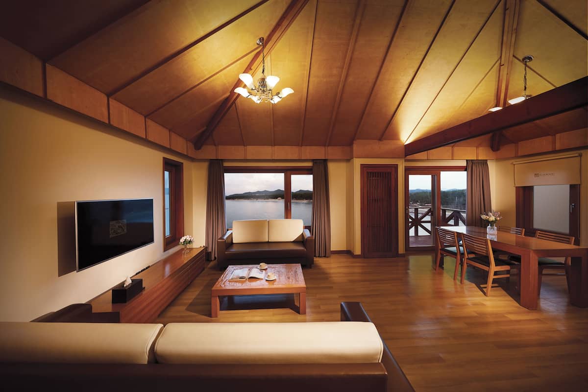 A spacious room with a wooden ceiling, a flat-screen TV, a sofa, a dining table, and a view of the outdoors.