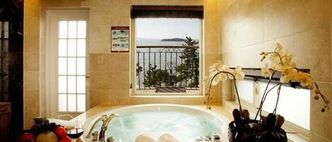A bathroom with a bathtub, a window with a view, a vase with flowers, and a towel rack.