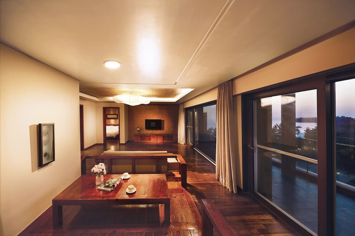 A modern interior with a wooden dining table, benches, a TV, and large windows.