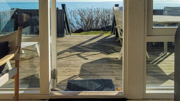 Una terraza de madera con vista al océano, un banco y una puerta que da a una habitación.