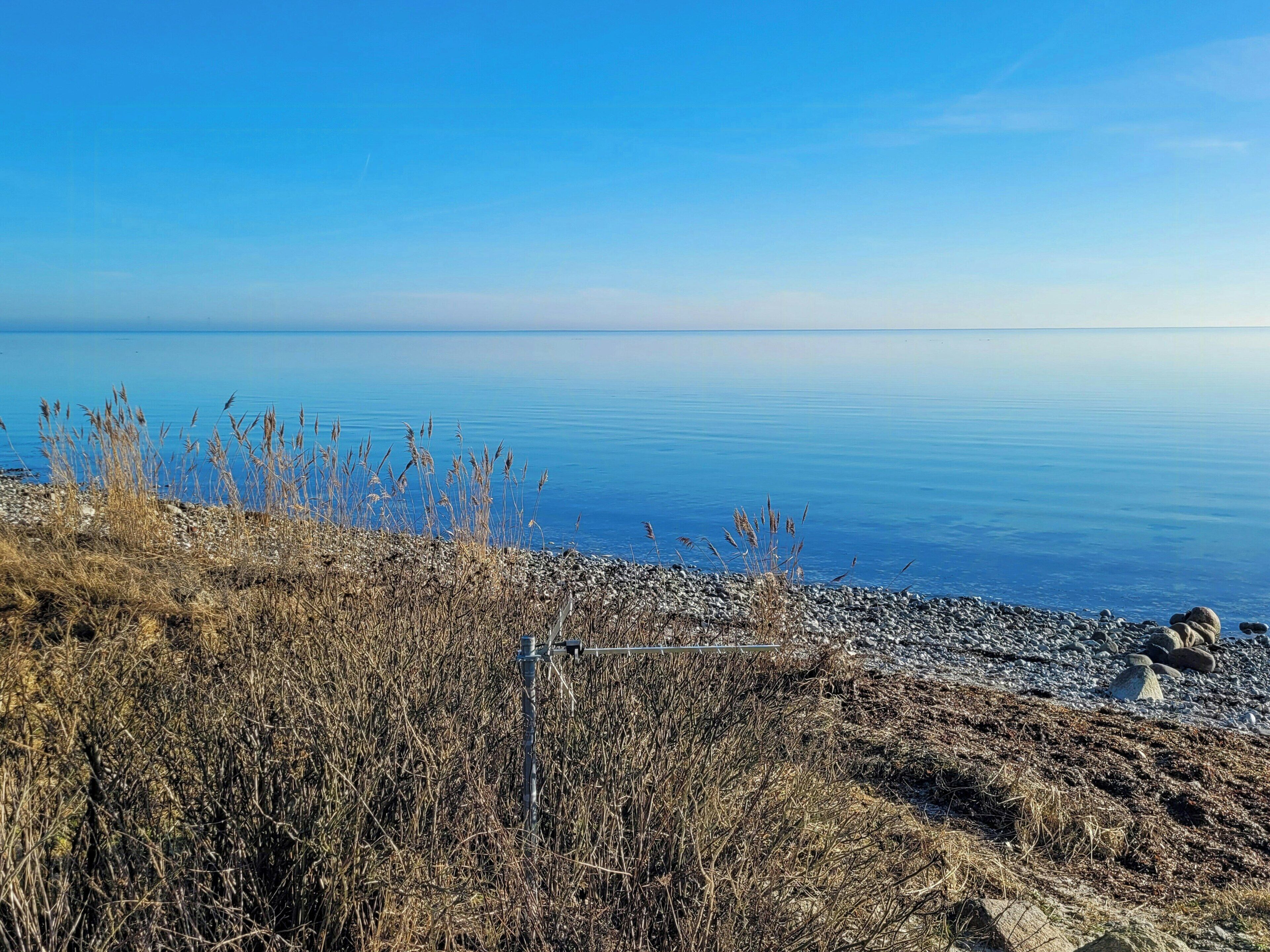 Eine Küstenlandschaft mit blauem Himmel, ruhiger See und felsigem Gelände mit vereinzelter Vegetation.