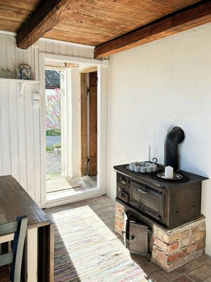A rustic kitchen with a wood-burning stove, a wooden table, and a door leading outside. - Rural guest house between Simrishamn and Skillinge (Simrishamn)