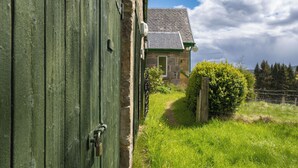 Un edificio rústico de piedra con una puerta verde, un camino de piedra que lo lleva hasta él y un seto en primer plano.