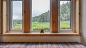 Una habitación con un banco, una ventana que ofrece vistas a un paisaje verde y un pequeño objeto de madera en el alféizar.