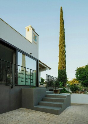 A modern building with a large window, a staircase, and a tall tree. - Contemporary villa among ancient olives in Puglia (Ostuni)