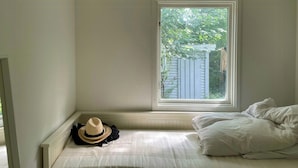 A bedroom with a window, a bed, and a hat on the floor.
