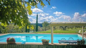Ein Swimmingpool mit Pergola, Gartenmöbeln und Blumentöpfen.