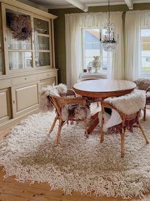 A room with a round wooden table, wicker chairs with fluffy cushions, a white shaggy rug, a glass-fronted cabinet, and a chandelier. - Charming farmhouse with open spaces near Österlen (Löderup)
