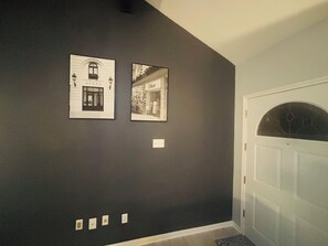 Ein Flur mit einer dunklen Wand, zwei gerahmten Bildern von Schaufenstern, einer weißen Tür mit Glasfenster und einer Fußmatte.