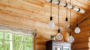 Un interior de madera con una mesa de comedor, sillas, lámparas colgantes y una ventana que ofrece vistas a árboles.