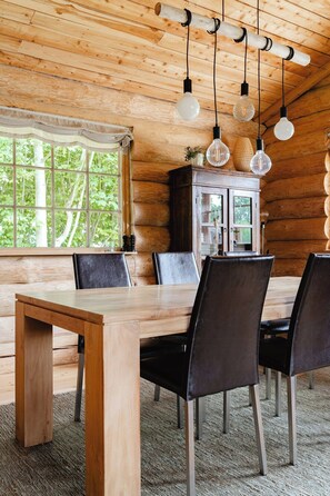 A wooden interior with a dining table, chairs, hanging light fixtures, and a window with a view of trees. - Modern log cabin by Dalby Huse beach (Dalby Huse)
