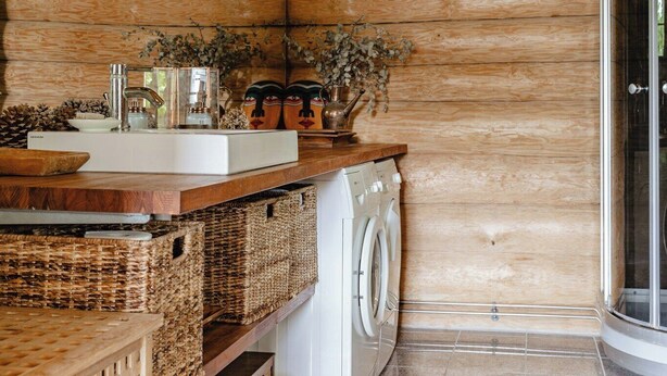Un interior de madera con lavadora, cestos de mimbre y un lavamanos.