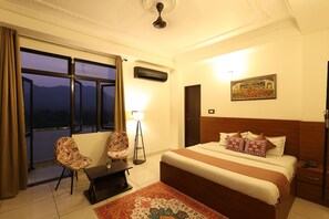 A hotel room with a bed, a desk, a chair, a lamp, and a window with curtains.