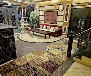 A hotel lobby with a red sofa, a round coffee table, a large potted plant, and a clock on the wall.