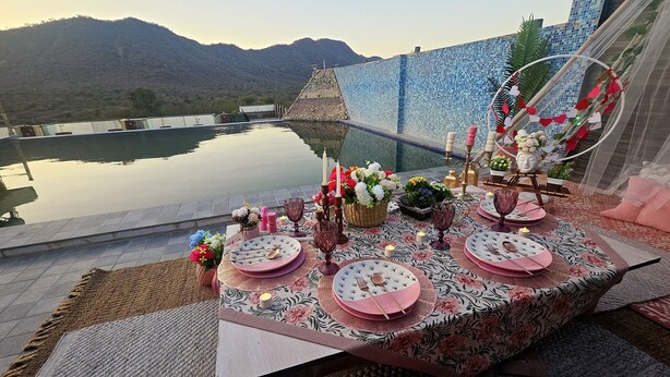 An outdoor dining setup with a view of mountains, a pool, and a decorative fence. - Hotel Ramgarh Palace (Jaipur)