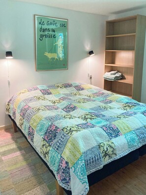Ein Schlafzimmer mit einer farbenfrohen gesteppten Bettdecke, einem hölzernen Bücherregal und einem gerahmten Poster an der Wand.