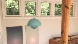 Un coin repas avec une table en bois, des chaises, un luminaire suspendu et une fenêtre donnant sur des arbres.