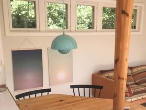 Ein Essbereich mit einem Holztisch, Stühlen, einer Hängelampe und einem Fenster mit Blick auf Bäume.