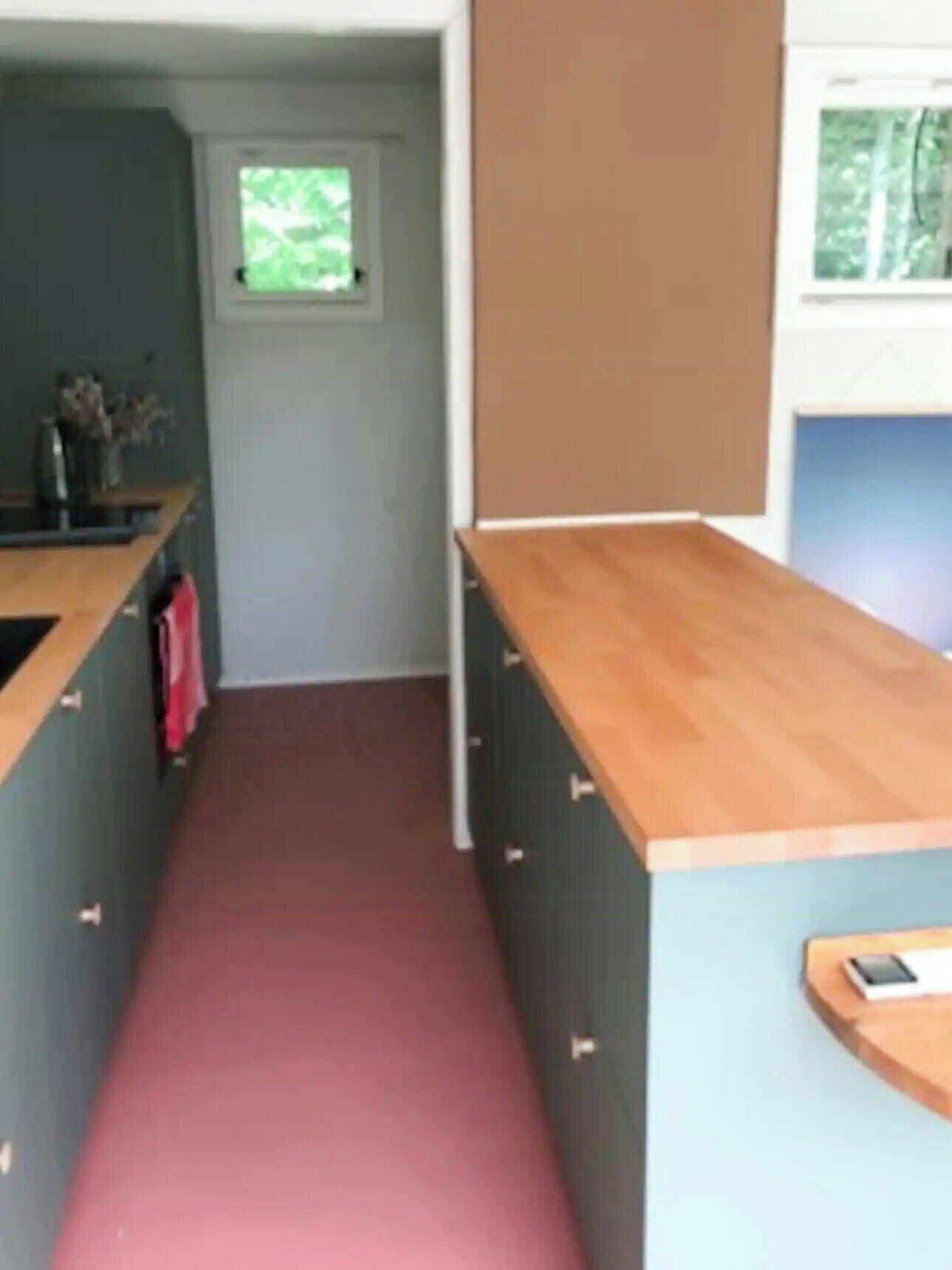 A narrow kitchen with a wooden countertop, grey cabinets, and a red floor.