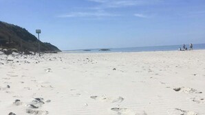 Une plage avec un ciel dégagé, un panneau indicateur et quelques personnes au loin.