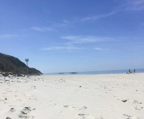 Ein Strand mit blauem Himmel, einem Wegweiser und einigen Personen in der Ferne.
