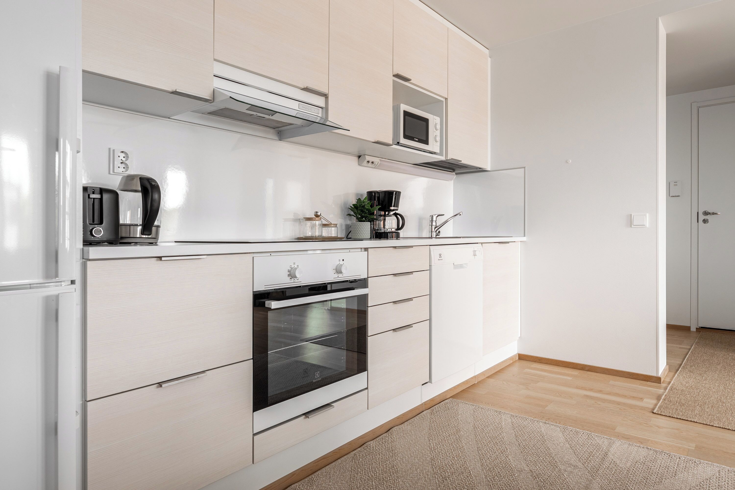 A modern kitchen with white cabinets, a built-in oven, a microwave, and a coffee maker.