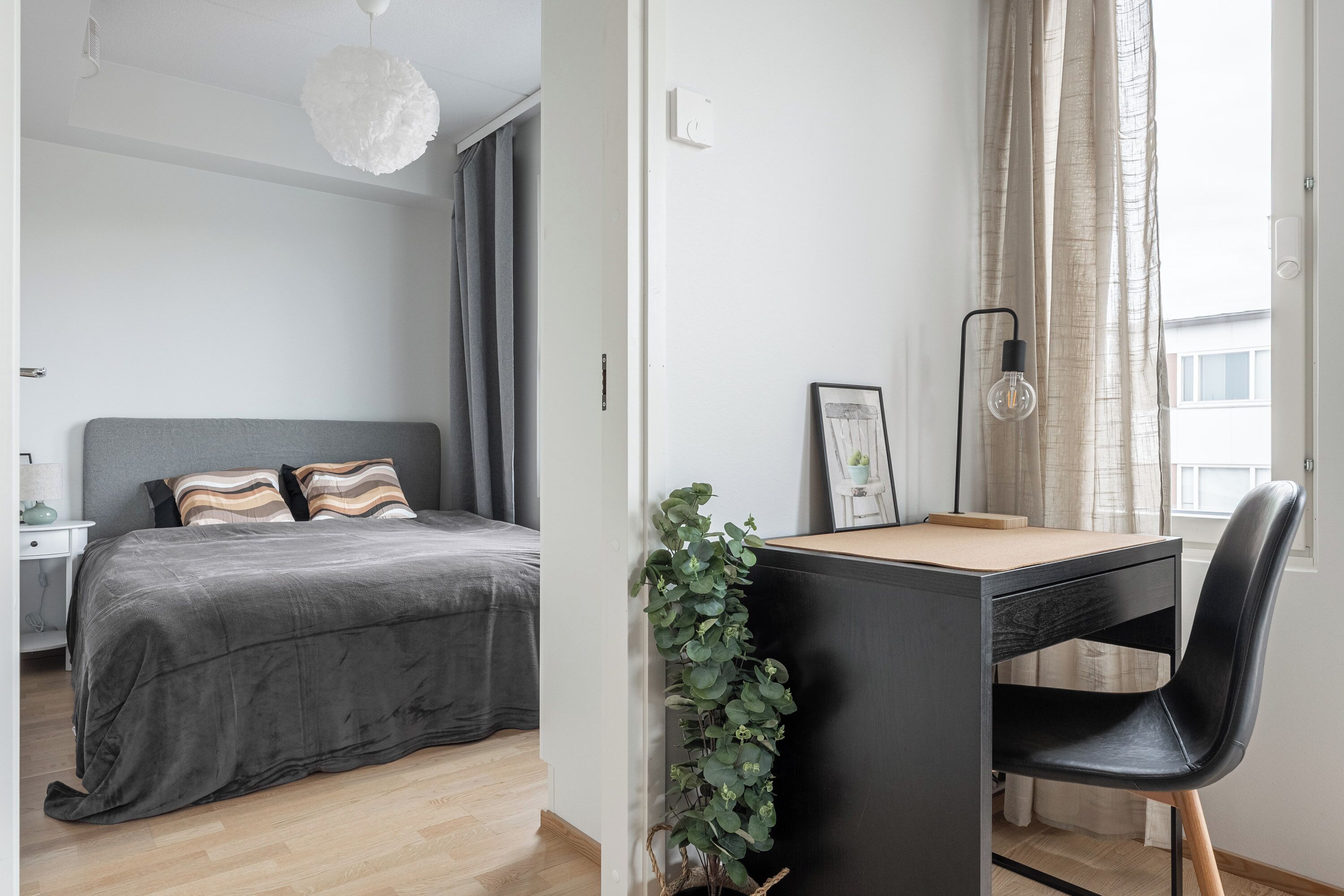 Un dormitorio con cama, mesita de noche, lámpara y vistas al exterior.