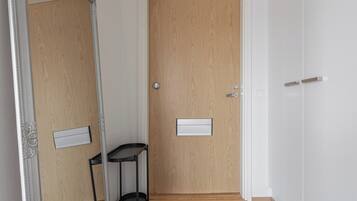 Un pasillo con una puerta de madera, un espejo, una mesita y un felpudo en el suelo.