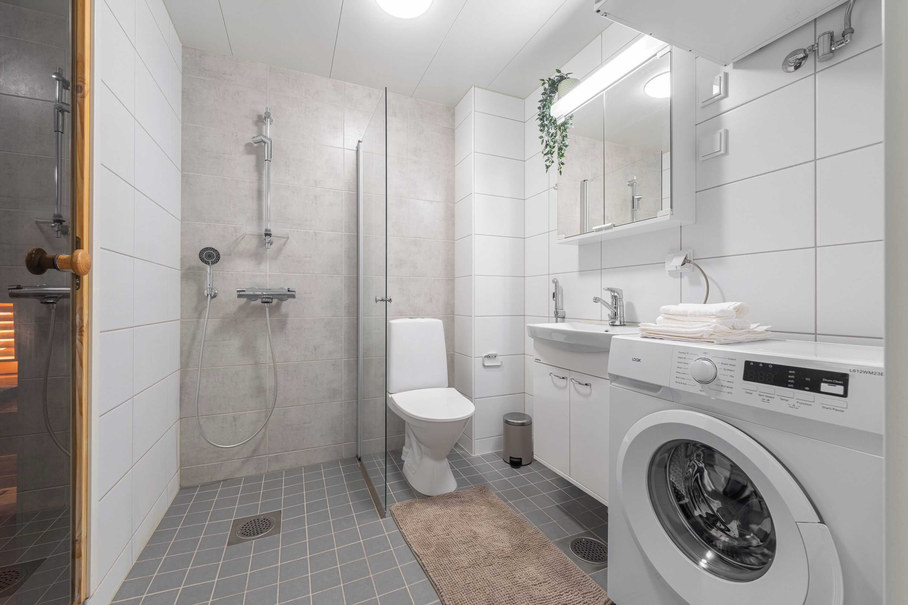 A modern bathroom with a glass-enclosed shower, a toilet, a washing machine, and a sink with a mirror.