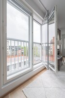 Una habitación con amplios ventanales correderos, piso de madera, alfombra blanca y un pequeño escritorio con lámpara.