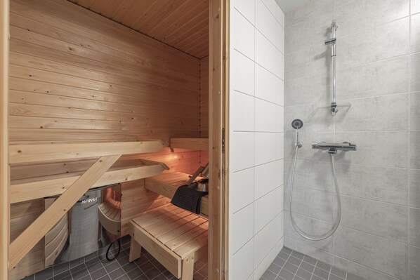 A sauna with wooden benches and a separate shower area with tiled walls.