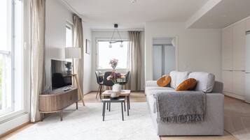 Een moderne woonkamer met een televisie, bank, eettafel en uitzicht naar buiten.
