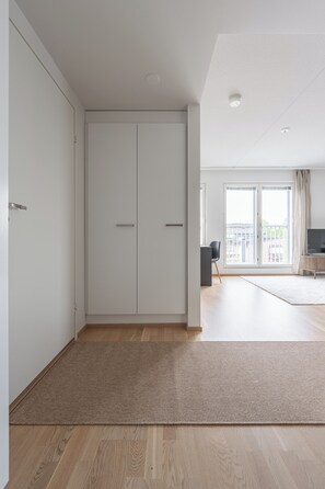 A modern living room with a large wardrobe, a flat-screen TV, and a view of the city through large windows.