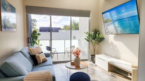 A modern living room with a sofa, a round coffee table, a TV mounted on the wall, and a balcony with a view. - Bright Turner Apartment with Parking and WiFi (Turner)